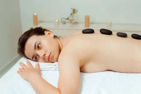Attraente donna con pietre calde sul retro sdraiato sul lettino da massaggio in spa — Foto stock
