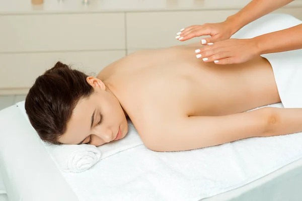 Vista ritagliata di massaggiatore facendo massaggio alla schiena per donna attraente in spa — Foto stock