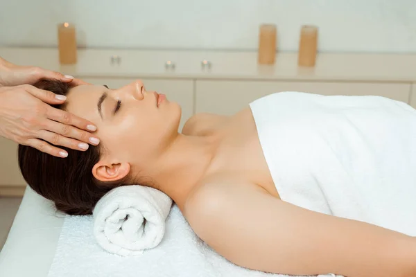 Cropped view of masseur doing face massage to attractive woman in spa — Stock Photo