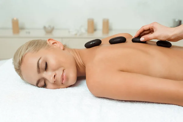 Cropped view of masseur doing hot stone massage to attractive woman in spa — Stock Photo