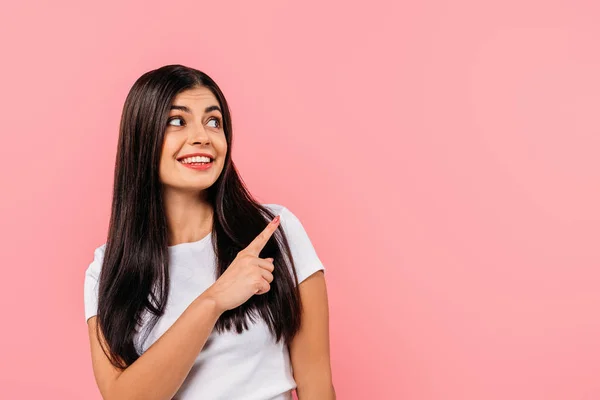 Sorridente bella ragazza bruna che punta con il dito lo spazio copia isolato sul rosa — Foto stock