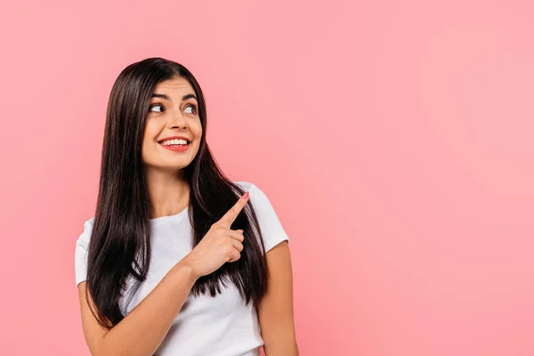 Sorrindo menina morena bonita apontando com o dedo no espaço cópia isolado em rosa — Fotografia de Stock