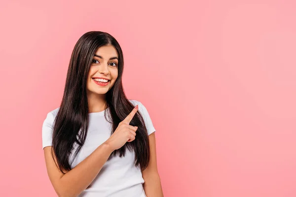 Lächelndes hübsches brünettes Mädchen, das mit dem Finger auf Kopierraum zeigt, isoliert auf rosa — Stockfoto
