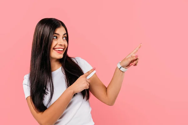 Sorridente bella ragazza bruna che punta con le dita lo spazio copia isolato su rosa — Foto stock