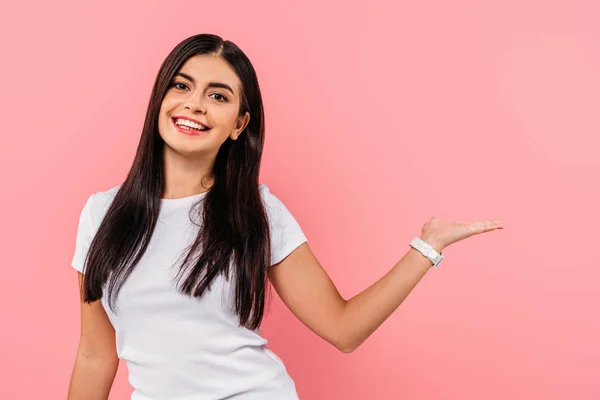 Smiling pretty brunette girl pointing with hand at copy space isolated on pink — Stock Photo