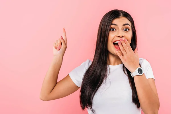 Excited pretty brunette girl with open mouth pointing with finger at copy space isolated on pink — Stock Photo