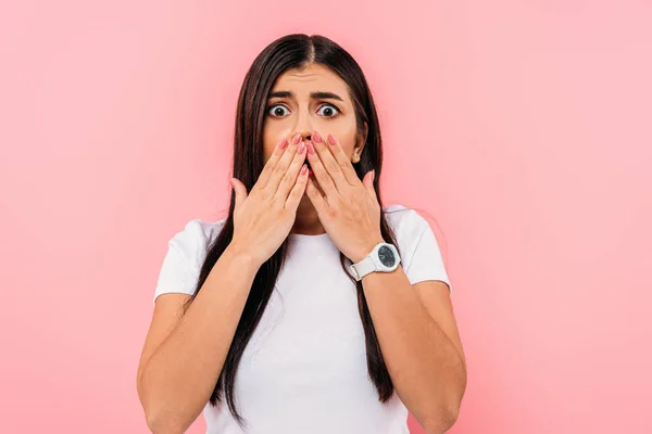 Scared pretty brunette girl covering mouth with hands isolated on pink — Stock Photo