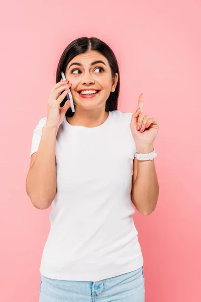 Lächelndes hübsches brünettes Mädchen, das auf dem Smartphone spricht und Ideengeste zeigt, isoliert auf rosa — Stockfoto