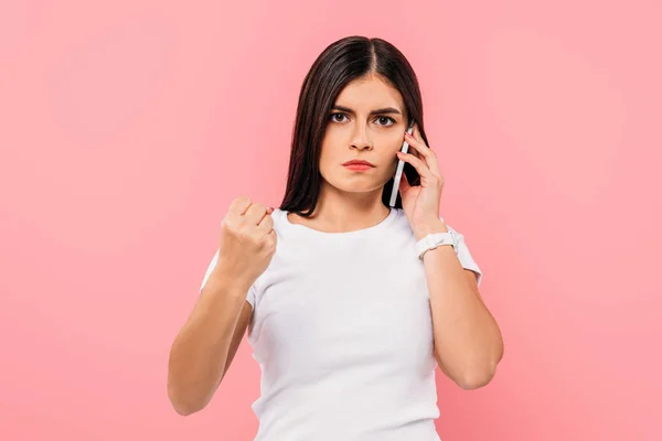 Wütendes hübsches brünettes Mädchen spricht auf Smartphone und zeigt Faust isoliert auf rosa — Stockfoto