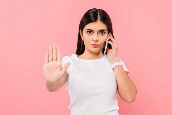 Bonita chica morena hablando en el teléfono inteligente y mostrando stop gesto aislado en rosa - foto de stock