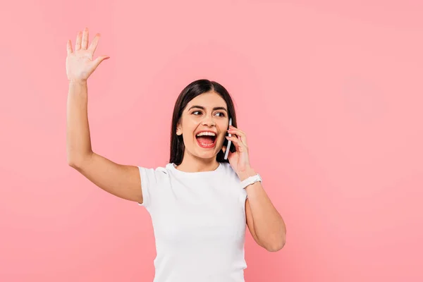 Excited pretty brunette girl talking on smartphone waving hand isolated on pink — Stock Photo