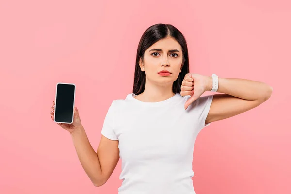 Sad pretty brunette girl holding smartphone with blank screen and showing thumb down isolated on pink — Stock Photo