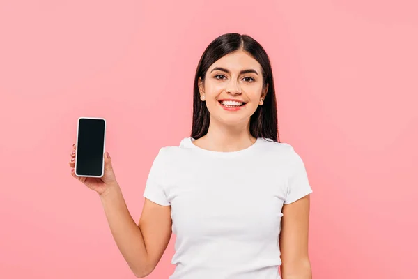 Sonriente chica morena bonita sosteniendo teléfono inteligente con pantalla en blanco aislado en rosa - foto de stock