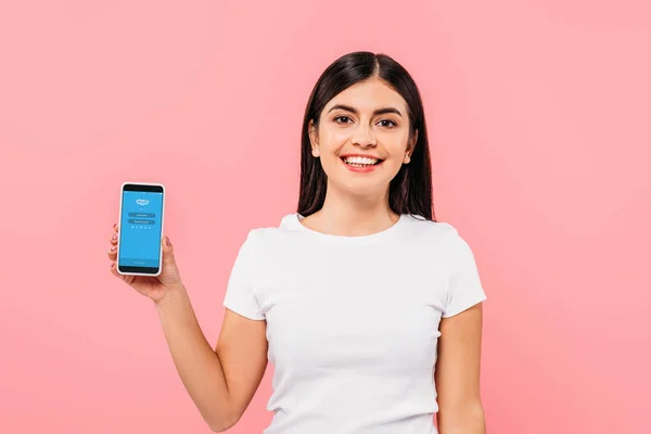 Kyiv, ukraine - 20. September 2019: lächelndes hübsches brünettes Mädchen mit Smartphone und Skype-App isoliert auf rosa — Stockfoto