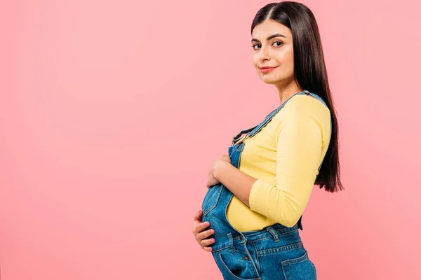 Side view of pregnant pretty girl touching belly isolated on pink — Stock Photo