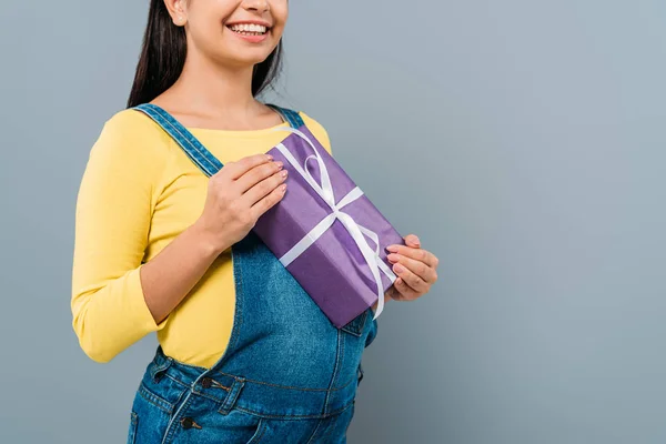 Abgeschnittene Ansicht eines lächelnden schwangeren hübschen Mädchens mit Geschenk isoliert auf grau — Stockfoto