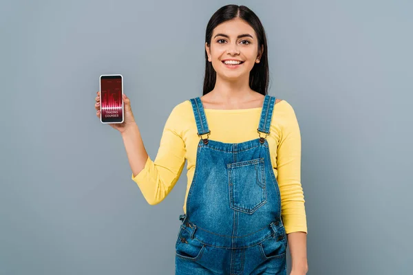 Lächeln schwangere hübsche Mädchen hält Smartphone mit Trading Courses App isoliert auf grau — Stockfoto