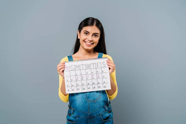 Усміхнена красива дівчина тримає календарний період ізольовано на сірому — стокове фото