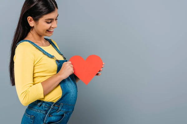 Side view of smiling pregnant pretty girl holding paper heart isolated on grey — Stock Photo