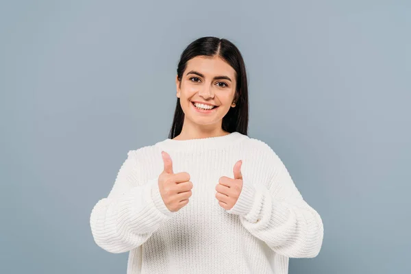 Happy pretty brunette girl in white sweater showing thumbs up isolated on grey — Stock Photo