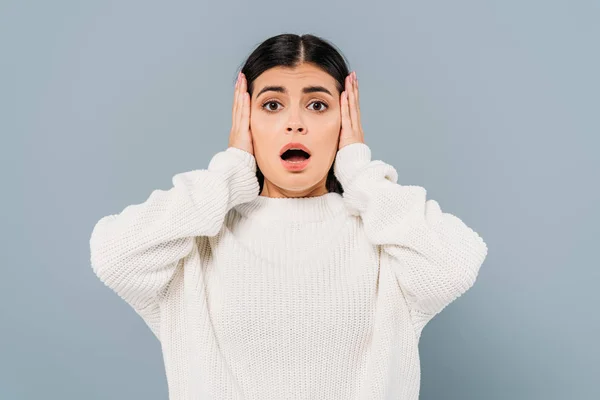 Shocked pretty brunette girl in white sweater covering ears isolated on grey — Stock Photo