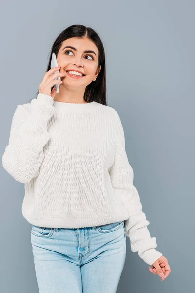 Lächelndes hübsches brünettes Mädchen im weißen Pullover, das auf dem Smartphone isoliert auf grau spricht — Stockfoto