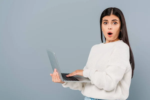 Shocked pretty girl in white sweater using laptop isolated on grey — Stock Photo