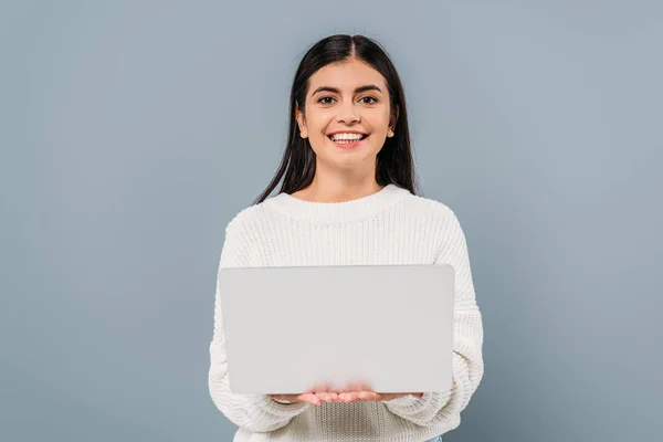 Sorridente bella ragazza bruna in maglione bianco che tiene il computer portatile isolato sul grigio — Foto stock
