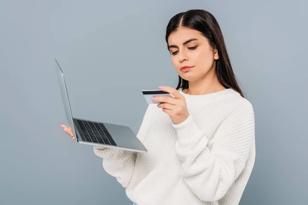 Menina bonita em camisola branca segurando laptop e cartão de crédito isolado em cinza — Fotografia de Stock