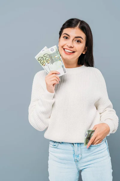 Niña bonita sonriente en suéter blanco sosteniendo billetes en euros aislados en gris - foto de stock