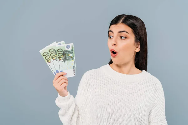 Impactado chica bonita en suéter blanco mirando billetes en euros aislados en gris - foto de stock