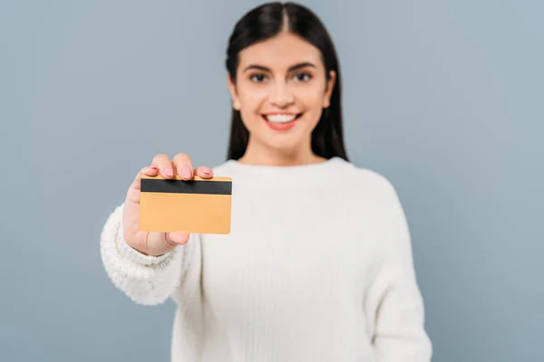 Enfoque selectivo de sonriente chica bonita en suéter blanco presentando tarjeta de crédito aislada en gris — Stock Photo