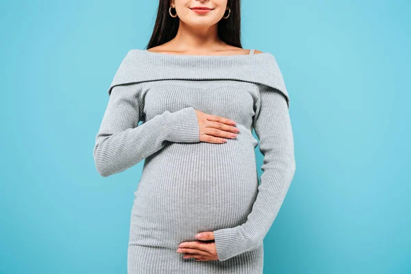 Corte vista de sorrir grávida bonita menina tocando barriga isolado no azul — Fotografia de Stock