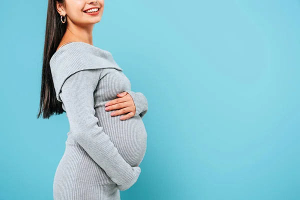 Side view of smiling pregnant pretty girl touching belly isolated on blue — Stock Photo