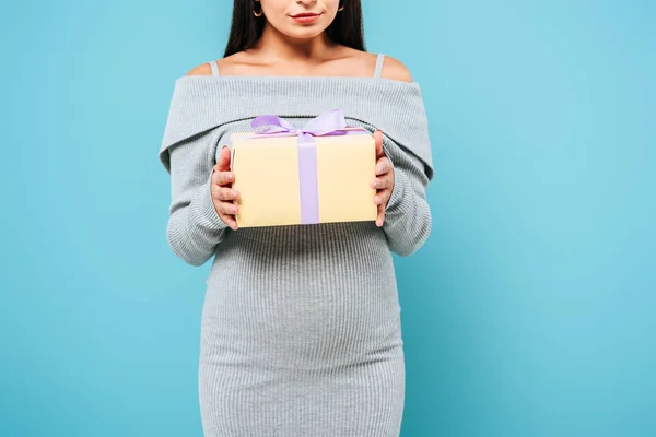 Partial view of pregnant pretty girl holding present isolated on blue — Stock Photo