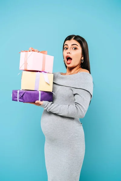 Шокована вагітна красива дівчина тримає подарунки ізольовано на синьому — стокове фото