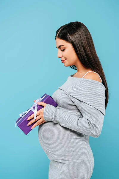Seitenansicht von schwangeren hübschen Mädchen hält Geschenke isoliert auf blau — Stockfoto