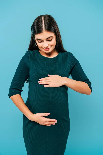 Lächeln schwangere Mädchen berührt Bauch isoliert auf blau — Stockfoto