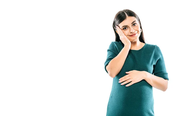 Sonriente chica embarazada tocando vientre y cara aislado en blanco - foto de stock