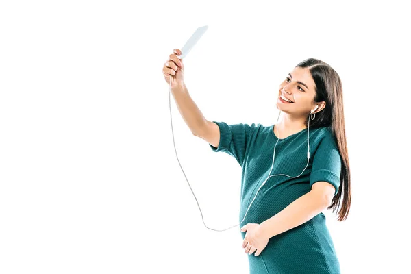 Sorridente ragazza incinta scattare selfie su smartphone e ascoltare musica in auricolari isolati su bianco — Foto stock