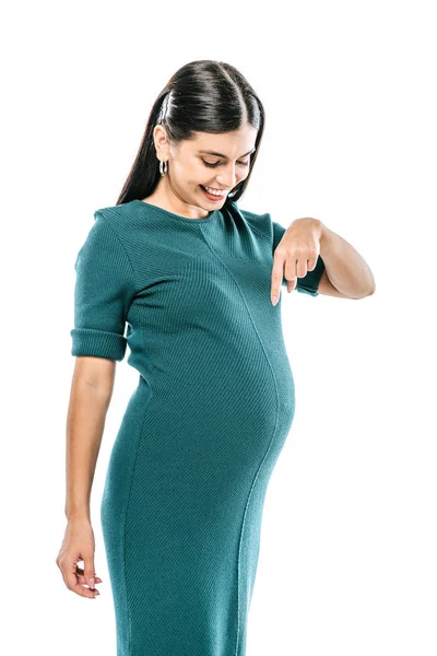 Усміхнена вагітна дівчина вказує пальцем на живіт ізольовано на білому — стокове фото