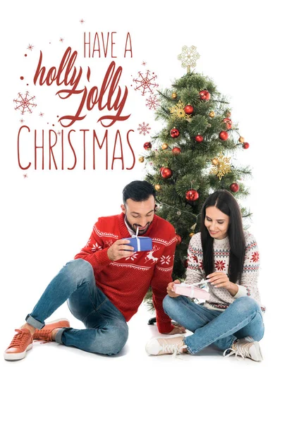 Cheerful man and happy woman holding gifts near christmas tree isolated on white with have a holly jolly Christmas illustration — Stock Photo