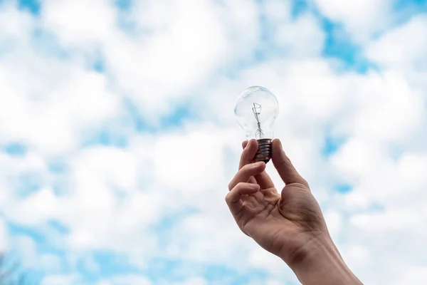 Cropped view of woman holding light bulb with blue sky and clouds on background — Stock Photo