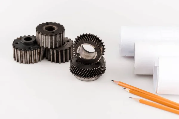 Metal round gears near rolled blueprints and pencils on white background — Stock Photo