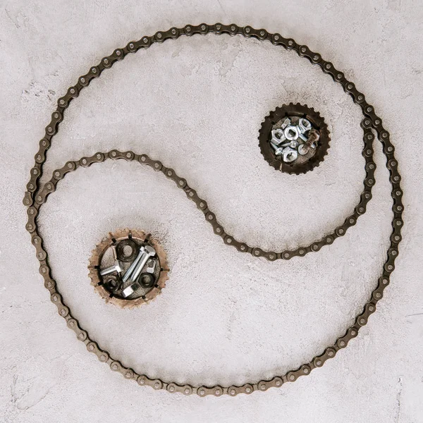 Vista superior de engranajes y tornillos de metal envejecido dispuestos en taijitu símbolo sobre fondo gris - foto de stock