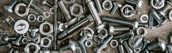 Top view of metal screws and nails scattered on grey background, panoramic shot — Stock Photo