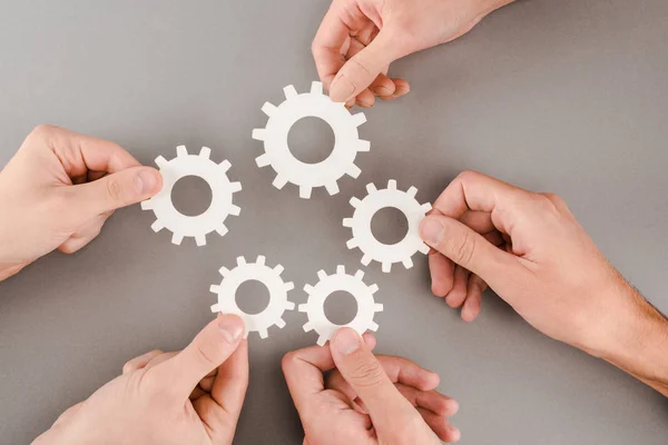 Cropped view of people holding white gears on grey background — Stock Photo