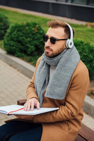Blind man in headphones reading book with braille font in park — Stock Photo