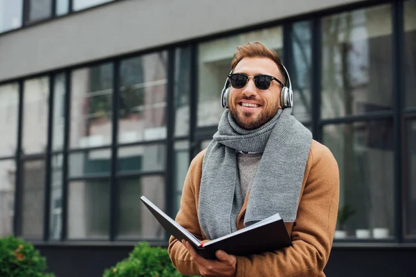 Усміхнений сліпий чоловік в навушниках тримає книгу на міській вулиці — стокове фото