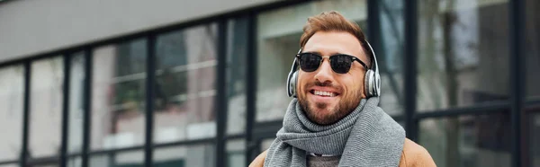 Panoramic shot of smiling man in sunglasses and headphones outdoors — Stock Photo